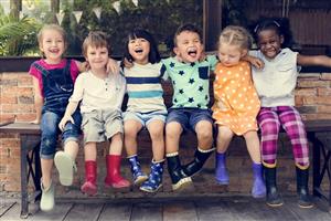 Kids laughing while wearing rainboots and sitting on a bench